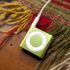 A green iPod Shuffle, a relic from when MP3 players were invented, rests on a wooden surface next to a colorful, fringed scarf.