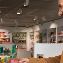 Uśmiechnięta sprzedawczyni w stena line sklepie bezcłowym prezentuje klientowi perfumy.