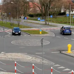 Samochody zbliżają się do ronda. Widoczny jest znak informujący o ruchu okrężnym, czyli kierunkowskaz na rondzie.