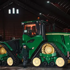 Man bredvid en stor grön John Deere-traktor i en lada. Frågan "hur länge håller diesel" kan vara relevant för denna maskin.