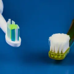 Głowica szczoteczki sonicznej obok zużytej szczoteczki manualnej na niebieskim tle.