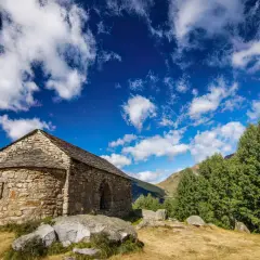 Pequeña ermita de piedra en las rutas del Vall de Boí, bajo un cielo azul con nubes algodonosas.