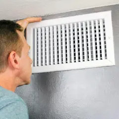Hombre revisa un conducto de ventilación, mostrando diferentes tipos de rejillas para el aire acondicionado.