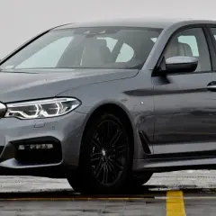 Szary sedan BMW Serii 5 G30 z czarnymi felgami, zaparkowany na mokrej nawierzchni.