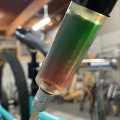 A syringe filled with red and green synthetic brake fluid, indicating a potential compatibility issue during a bike maintenance task.