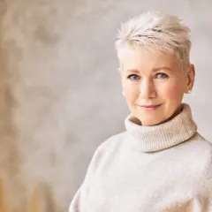 Kobieta z krótkimi, jasnymi włosami i niebieskimi oczami w beżowym golfie.