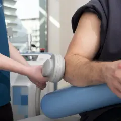 Fizjoterapeuta wykonuje zabieg rehabilitacji łokcia za pomocą specjalistycznego urządzenia.