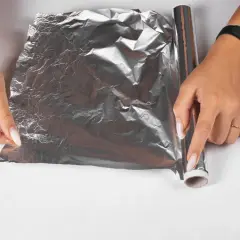 Dłonie rozwijają folię aluminiową, by zapobiec powstawaniu kożucha na sosie. Jak go zabezpieczyć folią?
