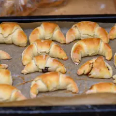 Upieczone, złociste kruche rogaliki z marmoladą, ułożone na blasze wyłożonej papierem do pieczenia.