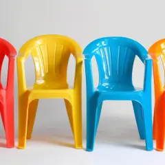 Cztery kolorowe plastikowe krzesełka: czerwone, żółte, niebieskie i pomarańczowe. Idealne do ogrodu, zastanawiasz się, czym pomalować plastik?