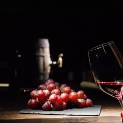 Czerwone winogrona i kieliszek wina, a w tle beczka. Czy wino bezalkoholowe ma alkohol? To pytanie nurtuje wielu miłośników tego trunku.