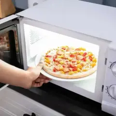 Ręka wkłada do mikrofali talerz z pizzą Giusseppe. Szybkie danie gotowe do podgrzania.