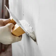 Manos con guantes aplican yeso a una pared. Pregúntate: cuanto tarda el yeso en secar para poder pintar.