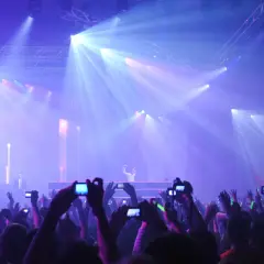 Tłumy na rave festivalu filmują DJ-a na scenie oświetlonej laserami.