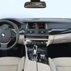 Wnętrze BMW F10 z jasną tapicerką, kierownicą, ekranem multimedialnym i panelem środkowym.