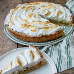 Tarte à la rhubarbe sur pâte feuilletée, recouverte d'une meringue dorée. Une part est servie sur une assiette.