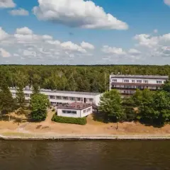 Budynki hotelowe w Ryni nad jeziorem, otoczone lasem i zielenią.