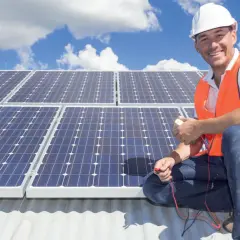 Uśmiechnięty monter w kasku i kamizelce sprawdza instalację fotowoltaiczną. Rozdzielnica do fotowoltaiki jest kluczowa dla prawidłowego działania systemu.