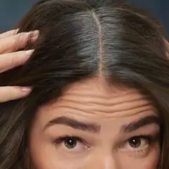 Mujer revisa su cabello oscuro con algunas canas. ¿Buscas como eliminar las canas para siempre?