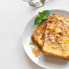 Dos rebanadas de tostada francesa dorada, bañadas en sirope y decoradas con menta. Una deliciosa french toast receta para el desayuno.