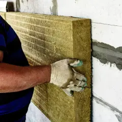 Pracownik montuje wełnę mineralną na ścianie. Utylizacja wełny mineralnej cena jest ważna przy planowaniu prac.