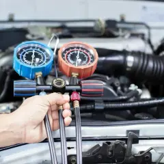 Mechanik sprawdza ciśnienie czynnika r1234yf w układzie klimatyzacji samochodu za pomocą manometrów.