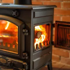 Płonące drewno w kozie do palenia drewnem, z uchyloną drzwiczkami, tworzy przytulną atmosferę.