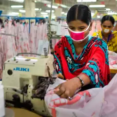 Frauen mit Masken arbeiten an Nähmaschinen. Sie sind Teil einer nachhaltigen Textilproduktion, die auf faire Arbeitsbedingungen und umweltfreundliche Prozesse setzt.