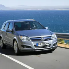 Srebrny Opel Astra H kombi jedzie drogą nad morzem.