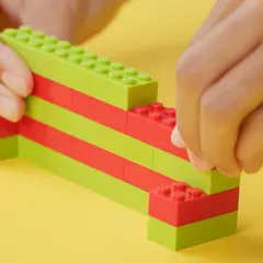 Dziecko buduje z zielonych i czerwonych klocków, pokazując, jak zbudować z klocków lego.
