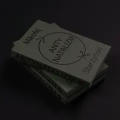 Stos książek z napisem "ANTY NATALIZM" i symbolem nożyczek. Dzieło Mikołaja Starzyńskiego.