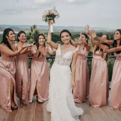 Panna młoda w białej sukni z bukietem i druhenki w różowych sukniach na tarasie.