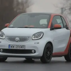 Biały Smart z pomarańczowymi akcentami na dachu i błotnikach. Zastanawiasz się, ile pali Smart? Ten model jest znany z niskiego spalania.