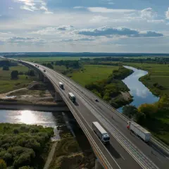 Most na Via Baltica przecina malowniczą dolinę rzeki, po której płyną ciężarówki.