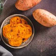 Chrupiące chipsy z batatów na talerzu, obok surowe bataty. Warto wiedzieć, jaki bataty indeks glikemiczny mają, by świadomie je spożywać.