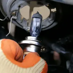 Ręka w rękawicy wymienia żarówkę reflektora samochodowego.