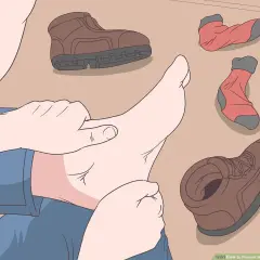 A person checks their foot, surrounded by hiking boots and socks, to prevent walking boots rubbing above the ankle.