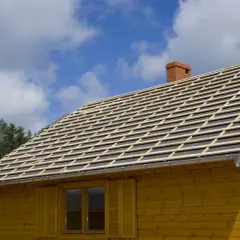Drewniany dom z nowym dachem w trakcie budowy. Widać łaty dachowe i komin. Zastanawiasz się, ile wypuścić dach poza obrys budynku?
