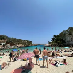 Słoneczna pogoda na Majorce, plaża pełna ludzi kąpiących się i opalających.