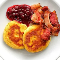 Två gyllene potatisbullar med knaperstekt bacon och rårörda lingon. Ett klassiskt potatisbullar recept som passar perfekt till helgfrukosten.