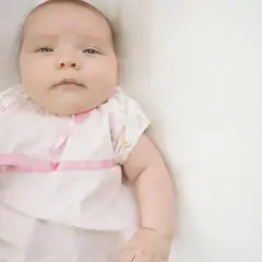 Dziecko z oznakami makrosomii płodu, ubrane w różową sukienkę z kokardkami, leży na białym tle.