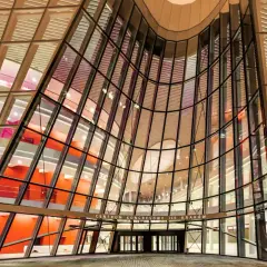 Nowoczesna fasada Centrum Kongresowego ICE Kraków z przeszklonym, falującym dachem i pomarańczowymi ścianami wewnątrz.