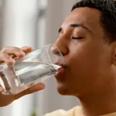 Un jeune homme boit un verre d'eau minérale magnésium, une boisson rafraîchissante et bénéfique.