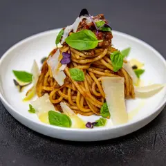 Pyszne spaghetti alla norma z sosem pomidorowym, bakłażanem, bazylią i parmezanem, podane na białym talerzu.