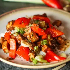 Leckeres, klebriges Tofu-Rezept mit Reis, Paprika und Frühlingszwiebeln, garniert mit Kräutern.