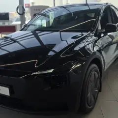 Błyszczący, czarny Tesla Model Y, idealny dla siedmioosobowej rodziny, stoi w salonie.
