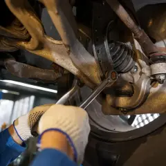 Mechanik dokręca śrubę w zawieszeniu samochodu kluczem.