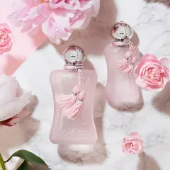 Dwa różowe flakoniki perfum de marly delina otoczone delikatnymi różowymi kwiatami i piwoniami.