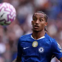 Piłkarz Chelsea w niebieskiej koszulce z piłką nad głową.