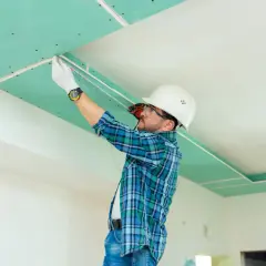 Operaio con casco misura il soffitto in cartongesso, pronto per lo stucco.